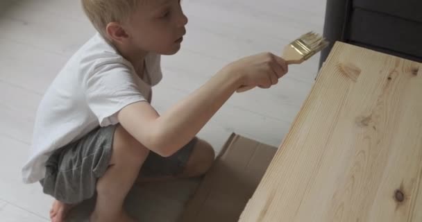 Il piccolo ragazzo biondo accuratamente copre il tavolo di vernice. Bambino aiuta con il lavoro di falegnameria. — Video Stock
