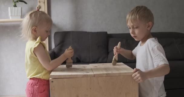 Los niños pintan cuidadosamente los muebles con pincel. Mesa de pintura con color blanco. — Vídeos de Stock