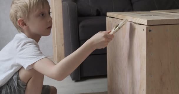 Mladý chlapec maluje stůl nezávisle. Kid nanáší ochranný nátěr štětcem. — Stock video
