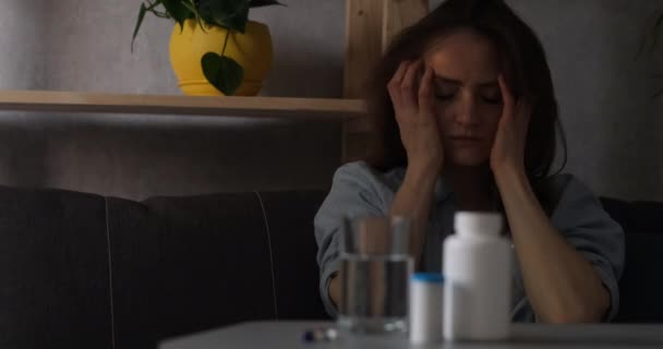 Una joven que sufre de dolor de cabeza, toca sus sienes. Píldora delante en la mesa. — Vídeos de Stock