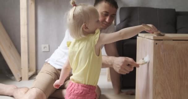 Ojciec i jego córki naprawiają i malują razem stół meblowy. Mała dziewczynka pomaga ojcu w warsztatach stolarskich. — Wideo stockowe