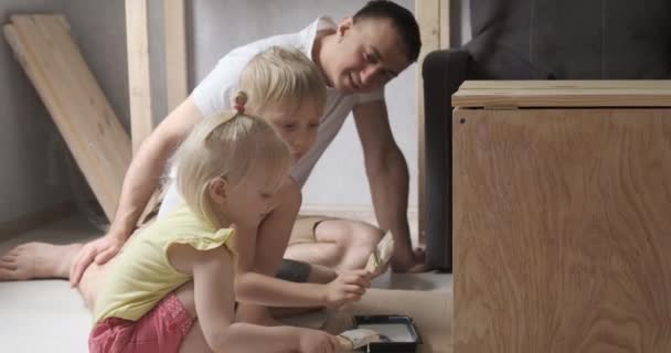 Father and little children paint carpentry together. Children help dad in workshop. — Αρχείο Βίντεο