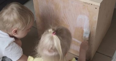 Children repair and paint together furniture. Little brother and sister applying protective coating.