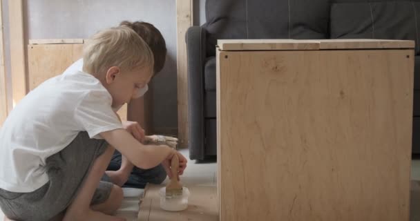Two friends applying paint to table with brush. Children help in carpentry workshop. — Stok Video