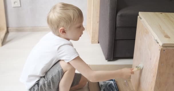 En sexårig pojke hjälper sin far i snickeriverkstaden. Barn som applicerar färg med borste. — Stockvideo