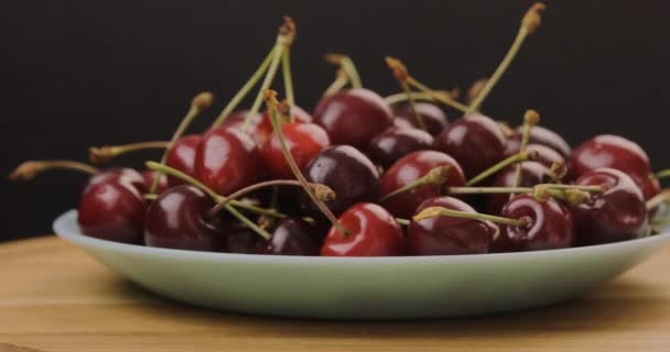 Talerz czerwonych wiśni na drewnianym stole. Pyszne dojrzałe owoce wiśni. Obrót o 360 stopni. Ruch pętli. — Wideo stockowe