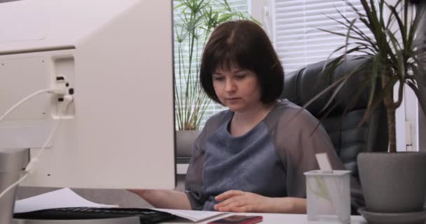 女人坐在电脑前的办公桌前看文件。编写工作报告. — 图库视频影像