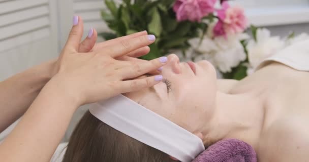 Masseur streelt het gezicht van een jong mooi meisje. Face Massage in schoonheidssalon. Professionele huidverzorging. Sluiten. — Stockvideo