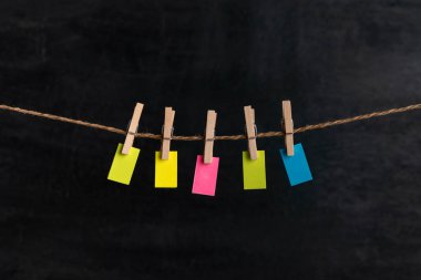 Small bright paper hang with clothespins on rope. Black background. Copy space. Place for your text