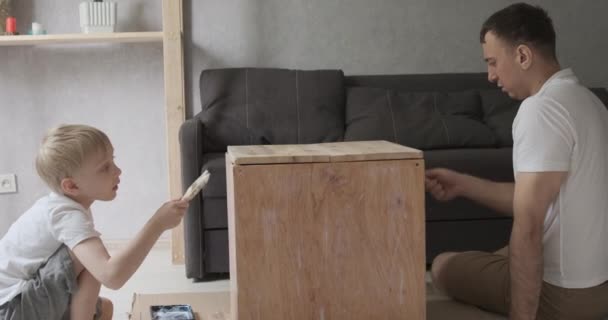 Papá e hijo reparan y pintan juntos muebles. Boy ayuda a papá en taller de carpintería. — Vídeo de stock