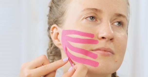 Spesialis menerapkan rekaman kinesio di wajah wanita muda untuk mengencangkan kulit. prosedur kecantikan Facelift. Fisioterapi dan Kinesiologi. — Stok Video