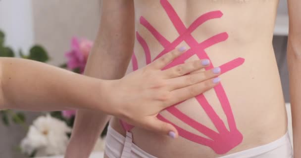 Terapeuten använder kinesioband på en ung kvinna i magen. Magsmocka med kinesiologi. — Stockvideo