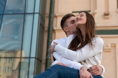 Young loving couple hugging in the background of urban architecture. Guy kissing his girlfriend.