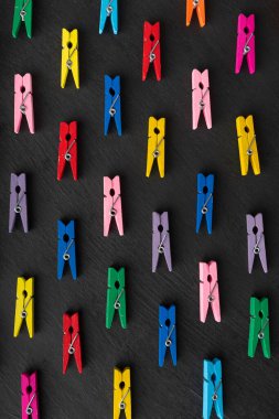 Multicolored clothespins on black background. Top view. Vertical frame.