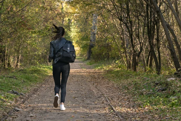 Girl runs along the park alley. Young woman runs away from someone in the park. Lonely girl in forest.