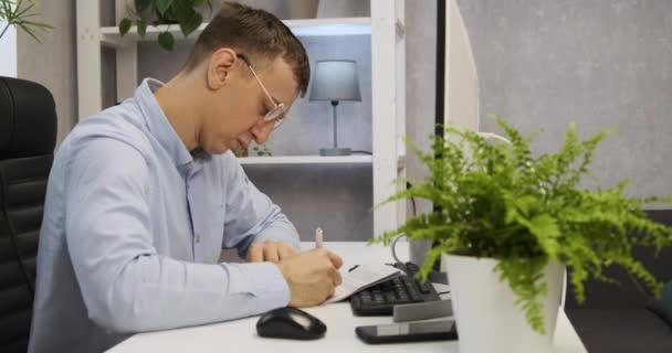 Un joven en el escritorio de la oficina está llenando el papeleo. Contable en el trabajo. Director firma los documentos. — Vídeos de Stock