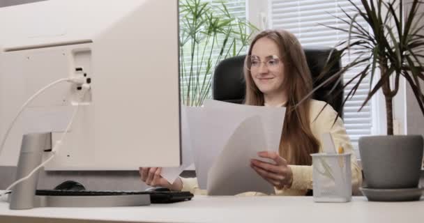 İş kadını masada oturuyor, belgeleri okuyor ve gülümsüyor. Genç bayan patron iş meselelerine ofiste karar veriyor.. — Stok video