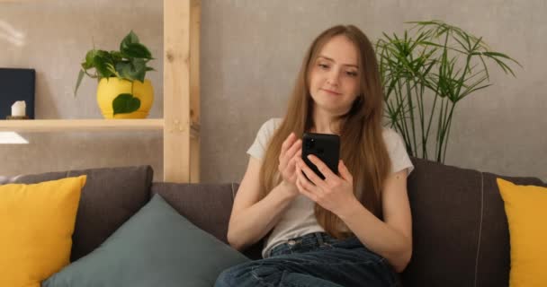 Femme lit les nouvelles sur Internet et est indignée. Fille en colère ennuyée regardant smartphone à la maison à l'intérieur. Demande ce que c'est — Video