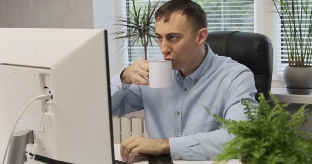 Un employé de bureau est assis au bureau, boit du café et regarde le moniteur. Directeur dans une chaise en cuir dans son bureau. — Video