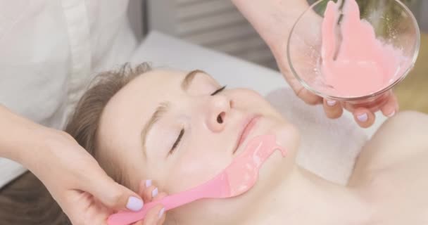 Esthéticienne applique un masque d'alginate sur le visage des patients. Fille en salon de beauté fait des traitements de beauté. — Video