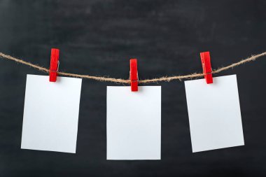Beyaz, boş kâğıt kartlar ipte mandallarla asılı. Siyah arka plan. Uzayı kopyala, maketle.