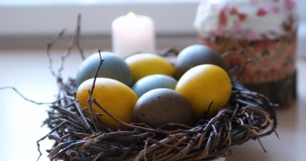 Bunte Ostereier im Vogelnest vor dem Hintergrund von festlichem Kuchen und Kerzen. — Stockvideo