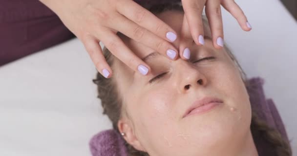 Hermosa joven en un masaje facial en un salón de spa. Procedimiento de belleza, modelando la cara ovalada. Salón de spa — Vídeo de stock