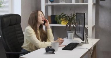 Masasındaki sekreter kız telefonda konuşuyor ve gülümsüyor. Görevdeki genç iş kadını..