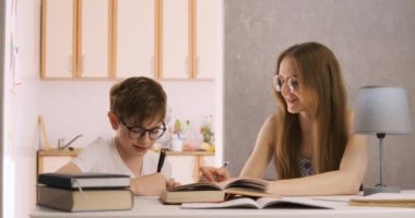 Anne ve oğul ev ödevi yapıyorlar. Genç öğretmen öğrenciyle çalışıyor. Öğretmen konuyu çocuğa açıklıyor.