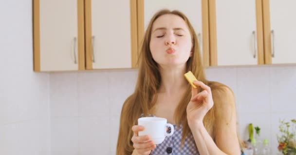 Κορίτσι πίνει τσάι με μπισκότα και χαμογελά όμορφη. Νεαρή γυναίκα τρώει κράκερ και απολαμβάνει τη ζωή. Απατεώνα. — Αρχείο Βίντεο