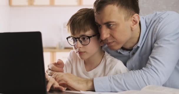 El joven padre ayuda a su hijo a hacer los deberes en la computadora. Aprendizaje a distancia con portátil. Clases en línea. — Vídeo de stock