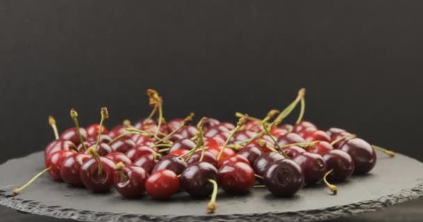 Placa rotativa preta com cerejas vermelhas maduras. Bagas sazonais maduras. Fundo preto — Vídeo de Stock