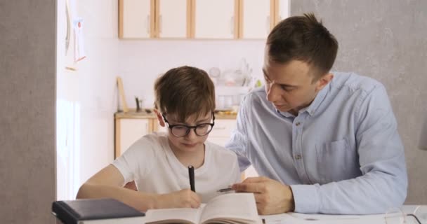 Papá ayuda a su hijo a hacer la tarea. El chico está haciendo los deberes con su padre. Profesor trabaja con estudiante en casa. — Vídeo de stock