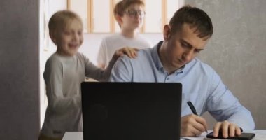 Çocuklar babalarının dikkatini dağıtıyor. Genç erkek serbest çalışan iki çocukla evde çalışmaya çalışıyor..