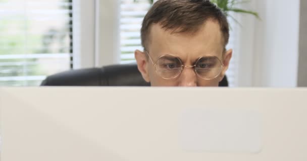 Mannen med glasögon arbetar på kontoret och tittar noga på monitorn. Kontorsarbetare arbetar intensivt. — Stockvideo