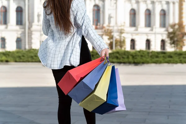 女の子のバックビューは 通りに沿って歩いて多色のショッピングバッグを運ぶ — ストック写真