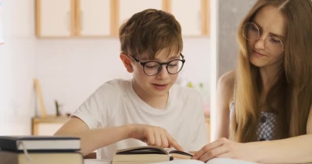 Estudante e professor estão lendo livro. A jovem mãe e o filho estão a fazer trabalhos de casa juntos. Tutor trabalha com estudante. — Vídeo de Stock