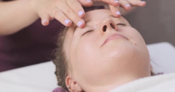 Young beautiful woman relaxes in the spa salon for a facial massage. Lymphatic drainage and modeling massage — Stockvideo