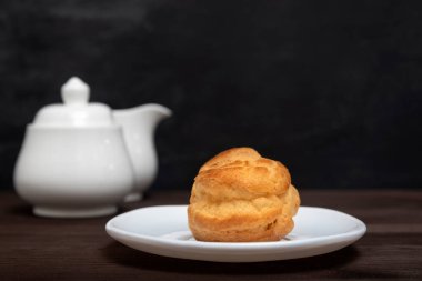 Ev yapımı profiterol, puf, popover, çaydanlık arka planında beyaz tabakta ekinoz.