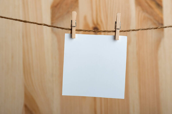 White blank sheet of paper hanging with clothespins on rope on wooden background. Copy space, mockup.