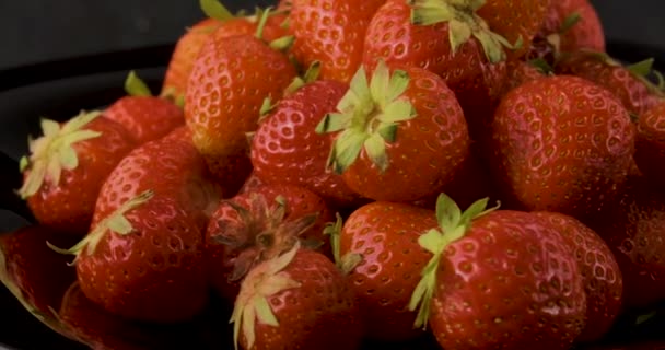 Cerrar fresas frescas maduras con hojas verdes sobre fondo negro. Cosecha de bayas de verano. Rotación de vídeo. Movimiento de bucle. — Vídeos de Stock