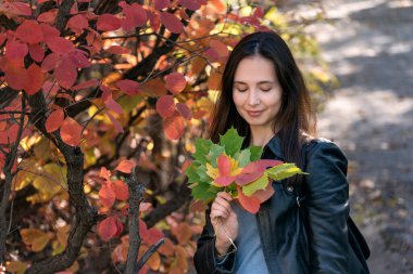 Parkta elinde bir buket sonbahar yaprağı tutan siyah saçlı kız. Ormandaki güzel genç kadın. Autumn Park