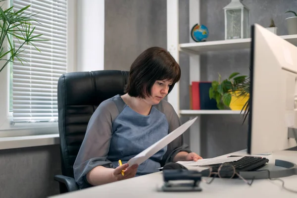 Woman chief in office works with documents and contracts. Employee prepares quarterly report. Director checks documents.