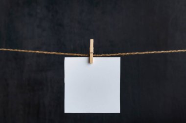 Siyah arka planda çamaşır mandallarıyla asılı boş kağıt kart. Uzayı kopyala Metnin için yer