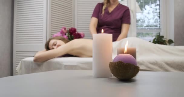 Glückliche junge Frau entspannt sich auf der Massageplatte in angenehmer Atmosphäre. Wellness Salon. Im Vordergrund brennende Kerzen — Stockvideo