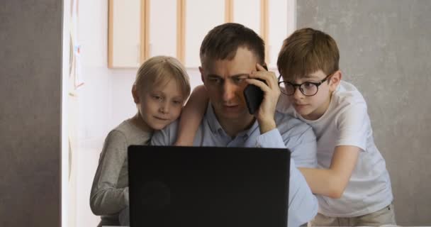 Батько розмовляє по телефону і працює в ноутбуці, два сини стоять поруч і відволікаються від роботи. Вільне і сміливе життя — стокове відео