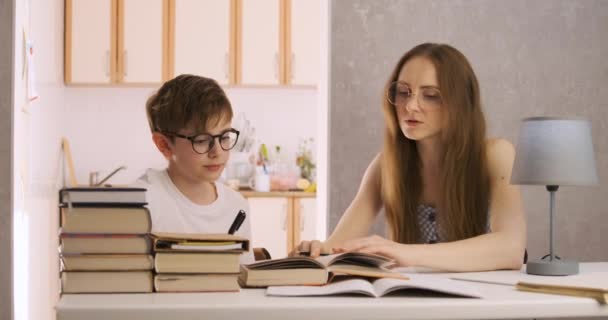 El joven profesor está estudiando con el estudiante. Madre e hijo están haciendo la tarea. Tutor explica el tema al niño. — Vídeo de stock