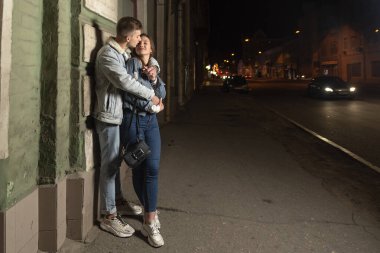 Adam kız arkadaşına sarılıyor, arka planda gece şehri. Akşam kentinde aşık mutlu genç bir çift. Sokakta romantik bir randevu.