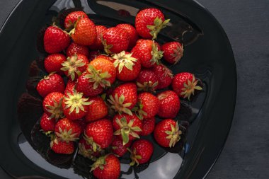 Siyah tabakta taze çilekler var. Mevsimlik meyveler. Kırmızı çilek