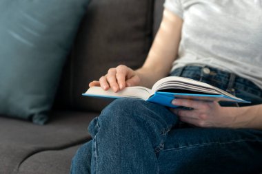 Kanepede otururken kitap tutan kadın. Kapatın. Kız evde kitap okuyor. Kadın ellerinde kitap..